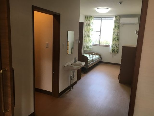 居室の洗面所とベッド 居室 ゆったりとした居室には、洗面所が備え付けられ、窓からは自然光が差し込む明るい空間です。窓辺には、休息できるベッドが配置されていて、快適な生活が送れることでしょう。