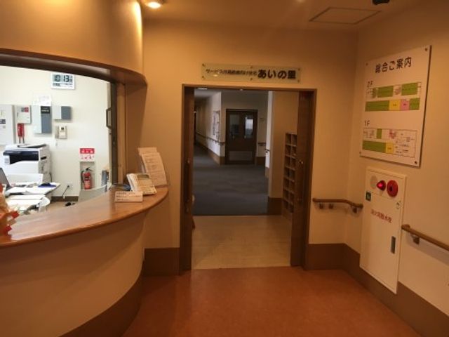 受付と廊下の一角 スタッフステーション 温かみのある色合いのロビーは、利用者様と家族が対話する心地よい空間を提供します。