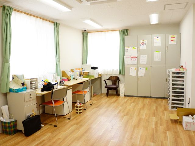 スタッフエリアの風景 最新のデータを事務所で管理 整理されたデスクと広告物が壁に貼られた明るいスペースです。就業の日々は、ここでのサポートや業務準備が始まります。