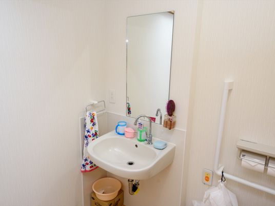洗面台周辺の壁には鏡やタオルハンガー、２口のコンセントが設置されている。石鹸や歯磨きセット等が用意されている。
