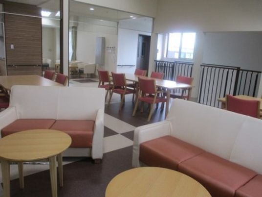 白色と茶色の模様の床に数組のテーブルや椅子やソファーが置いてある。黒い縦格子の柵が取り付けられている。