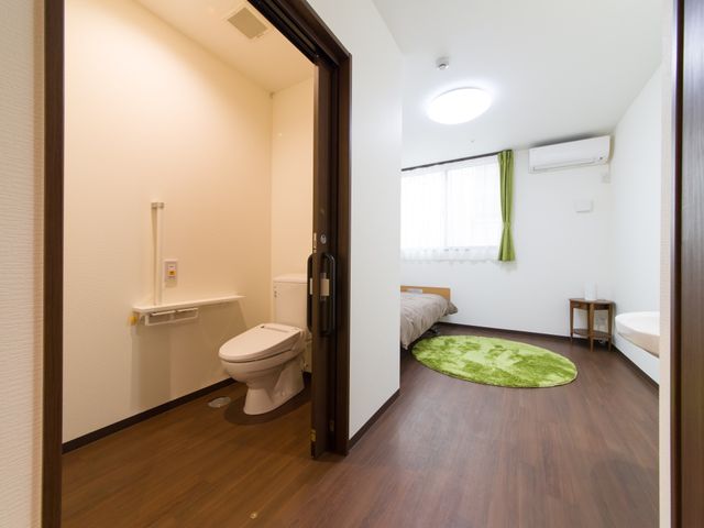 居室のトイレとベッド 居室 広々としてクリーンな居室には、必要な設備が整っており、快適な生活空間が提供されています。ベッドの横にはバリアフリー設計のトイレがあり、安心して過ごせます。