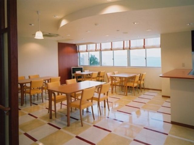 明るい快適な食堂 食堂兼機能訓練室 天井からの自然光が差し込む、広々とした食堂です。暖色の家具が温かみを与え、利用者様とのコミュニケーションも図りやすいでしょう。