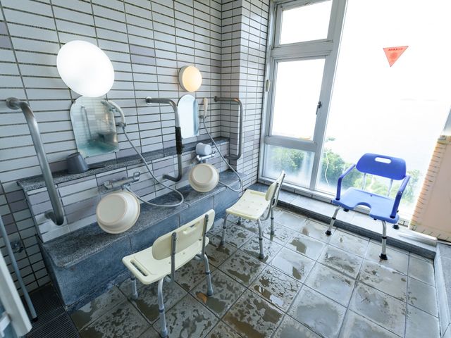 バリアフリー設計の浴室 浴室 手すりやシャワーチェアを備えた清潔な浴室は、利用者の安全と快適さを考慮して設計されています。窓から自然光が差し込み、開放的な雰囲気です。