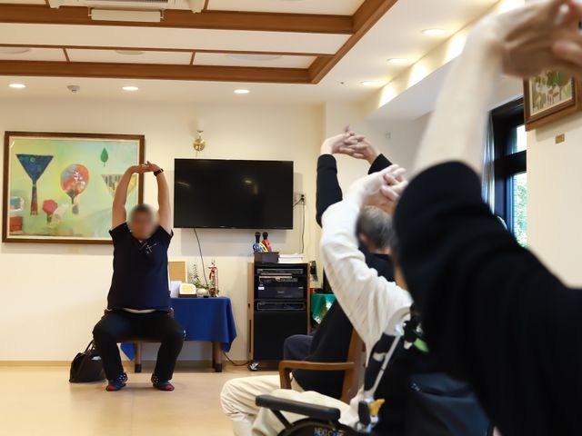 機能訓練の様子 共有スペース ゆったりした空間で行われる体操指導です。スタッフの温かいフォローがあり、ご利用者様の笑顔があふれています。