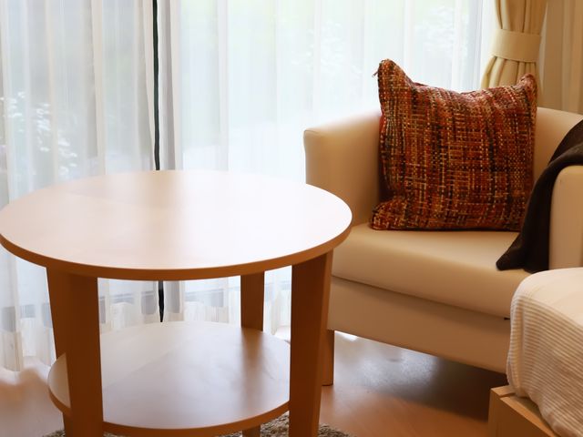 居室の円卓とソファ 個室 ゆったりとしたソファと丸いテーブルが配置された部屋です。窓辺の明るい光が穏やかなひとときを約束します。