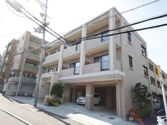 ベージュ色の建物の正面外観 外観 落ち着いた色合いのモダンな建物が迎えるエントランスです。清潔感があり、心地よい職場環境を予感させます。