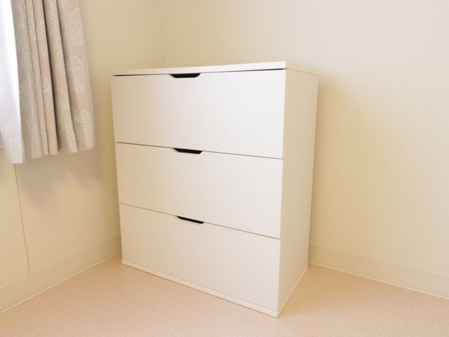 シンプルな洋室のタンス 収納 スッキリとしたデザインの居室用タンスがあり、個人の荷物を整理して保管することができます。明るい壁と調和しており、快適な空間を演出しています。