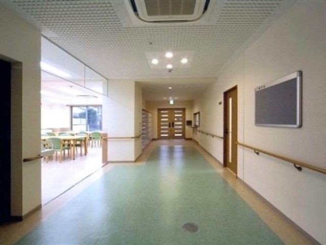 広々とした明るい廊下 廊下 手すり付きの廊下が広がり、安全かつ快適な移動が支援されています。奥には開放的な食堂が見え、交流の場へと誘います。
