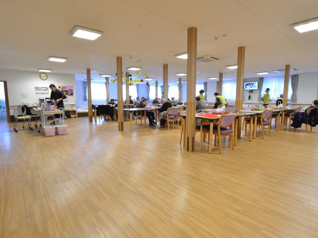 広々とした明るい食堂 食堂で過ごす利用者とスタッフ ゆったりとした食堂で、利用者様が食事や憩いの時間を過ごされています。スタッフも明るくサポートしており、和やかな雰囲気が伝わります。