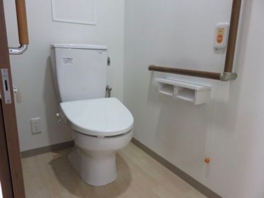 施設の写真 トイレは車椅子でも出入りが楽なスライドドアで、転倒防止の手すり、非常用の呼び出しボタンも備え付けられている。
