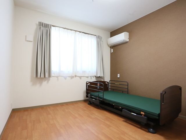 居室のベッドと窓 居室 シンプルで清潔感のある居室です。必要最低限の家具が整っており、心地よい空間を提供しています。