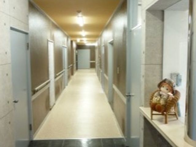 明るく清潔な廊下 受付 ゆったりとした通路が確保されており、スタッフや入居者の移動がしやすい設計です。壁面の飾り棚には心和む小物が置かれ、温もりを感じさせる空間となっています。