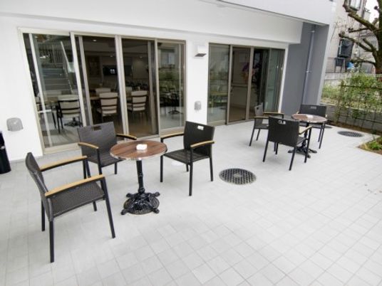 施設の写真 白の壁面と床、シックな黒と茶色のイス、テーブルが配置されモダンな雰囲気。比較的広いスペースのため、歓談以外にもさまざまな用途に使える。