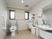 サムネイル 施設の写真 トイレは広々としていて手前に白い洗面台が設置されている。便器には背もたれと肘掛けが取りつけられている。
