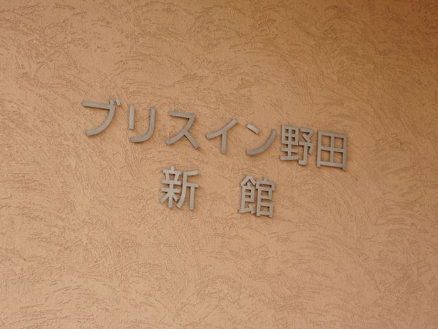 壁に取り付けられた看板 施設名 心温まる空間へ案内する、品がある入口の表札です。