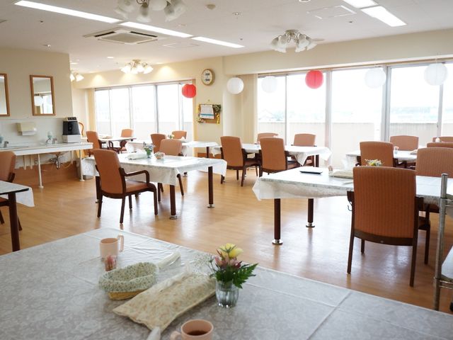 明るい食堂の様子 リビングダイニング 窓辺に並ぶテーブルで、ゆったりとした食事の時間を提供します。天井の照明と和風の飾りが心地よい空間を演出。