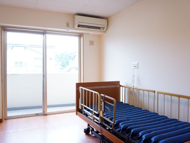明るい部屋のベッドと窓 居室 ベッドのそばに大きな窓があり、光がたっぷりと差し込む部屋です。安全を考慮した柵がついたベッドが心地よい安息を約束します。
