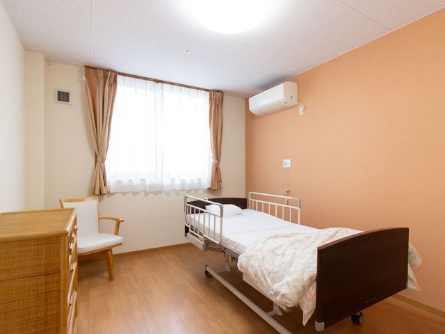 居心地の良い居室風景 居室 落ち着いた色合いの居室で、ベッドとテーブルが配置されており、ゆったりとした時間を過ごせそうです。窓からは自然光が差し込んでいます。
