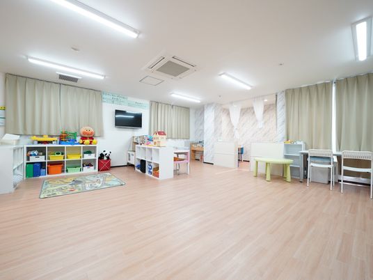 児童デイサービス内には、フローリングの床で統一された広い保育室が設けられている。白い棚には、子ども用のおもちゃなどが収納されている。