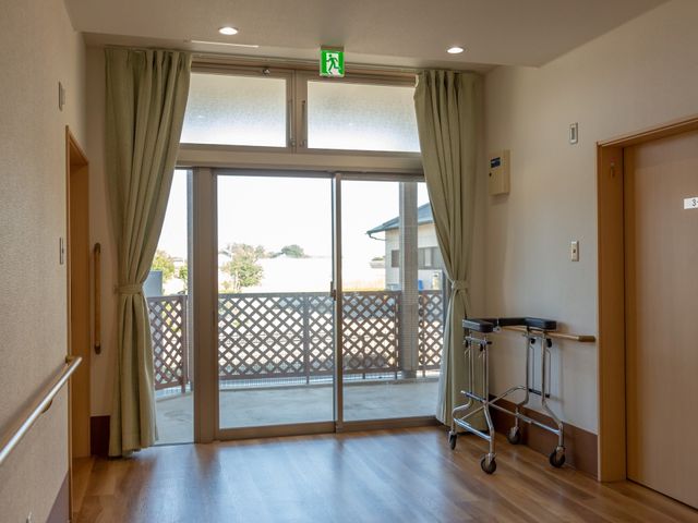 居室のバルコニーへの出口 廊下 広々とした居室の出口からは、明るい陽光が差し込むバルコニーがあります。歩行器を使っても安心して出入りできる設計です。