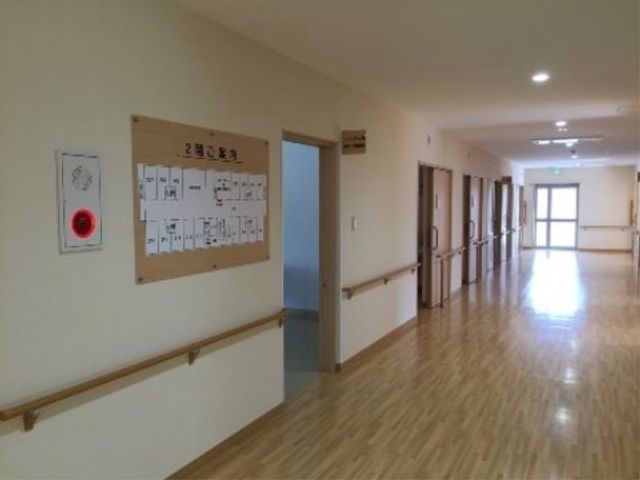 清潔感のある明るい廊下 廊下２ 手すりが設置された広々とした廊下は、採光が良く、歩行のサポートも万全です。壁面には施設の案内図も掲示され、安心してお過ごしいただける環境が整っています。