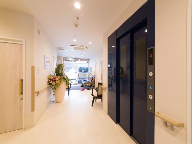 エレベーター付近の廊下 玄関 花が飾られたエントランス付近の廊下は、明るく開放感があります。職員とのやり取りも円滑に行える設計です。