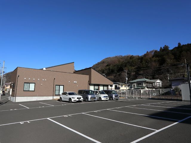 茶色の建物と駐車場 駐車場 青空の下に佇む落ち着いた色合いの建物は、広々とした駐車スペースを備えています。通勤にも便利な環境が整っております。