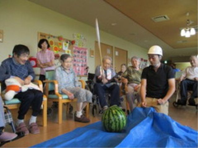 楽しいレクリエーション活動 夏祭り スイカ割りを楽しむ明るいレクリエーションの風景です。参加されている方々の笑顔が印象的で、活気が感じられます。