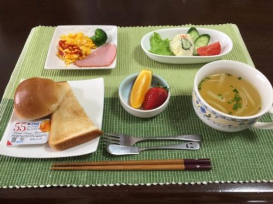 緑と黄緑でデザインされたランチョンマットの上に、パン、スープ、サラダ、スクランブルエッグ、果物が置いてある。