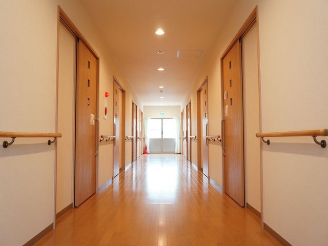 明るく清潔感のある廊下 通路 床に映る光が廊下全体を照らし、訪れる方々に温かい印象を与えます。手すりが設置され、安心して歩行できる空間です。