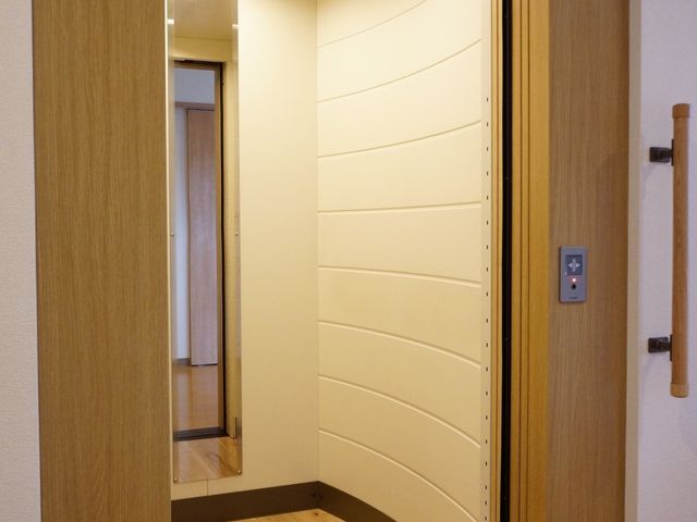 木目調の洋風窓枠 エレベーター 温かみのある木目調の窓枠が特徴的な居室です。落ち着いたデザインで、のびのびとした時間を過ごせます。