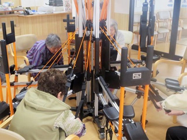 利用者の活動支援訓練室 リハビリ風景 明るく開放的な空間で、利用者がリハビリ機器を使用している様子が見られます。そこで働くことで、健康維持のお手伝いができます。