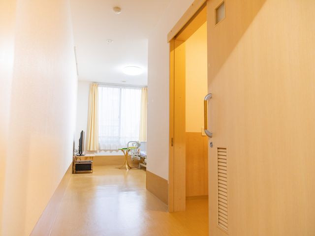 明るい個室の居室 居室 自然光が差し込む居室は、リラックスできる空間です。柔らかな色合いの床と壁が特徴です。