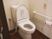 引き戸で広いスペースが確保されたトイレである。立ち座りがしやすいように壁に手すりが設置されており、緊急時の呼び出しボタンも付いている。