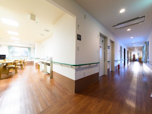 明るい廊下と食堂の一角 通路 広々として明るい廊下が見え、手を触れやすい手すりが備わっています。奥には食堂があり、ゆったりとした時間を過ごすことができます。