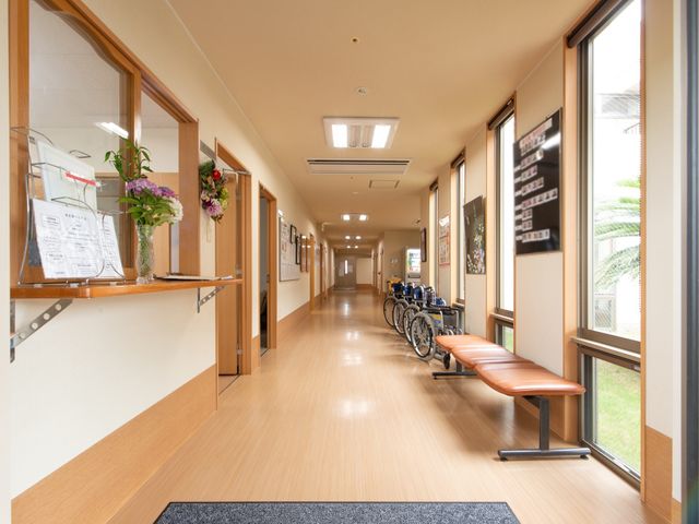 廊下に車椅子とベンチ ホール 広々とした廊下は、木目調の暖かい雰囲気を醸し出しており、ゆったりとした移動やくつろぎの時間を支えます。