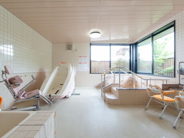 バリアフリー浴室設備 大浴場 手すりや椅子が備えられた清潔な浴室で、安全に心地よい入浴が実現されています。光が差し込む窓からは緑を望め、リラックスした時間をお過ごしいただけます。