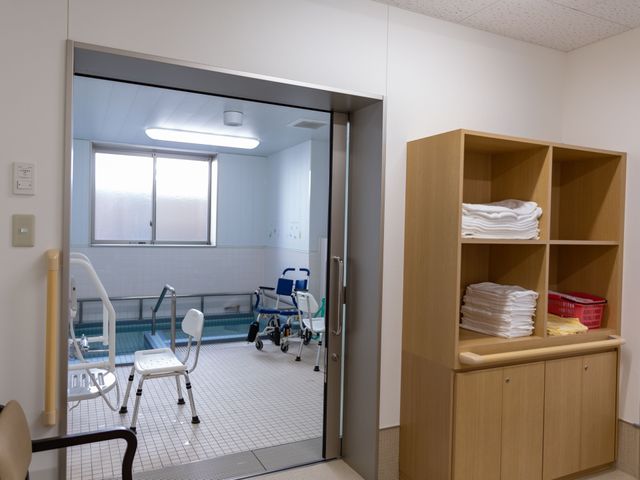 清潔な浴室と棚 脱衣所 安全に配慮された設計の浴室スペースです。手すりやシャワーチェアが配備され、快適な利用が可能です。