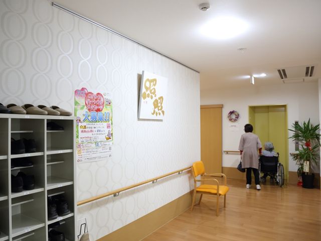 エントランス周りと利用者 玄関ホール 温かみのあるエントランス周りです。スタッフが優しくサポートしながら、利用者が次の活動へと移動しています。