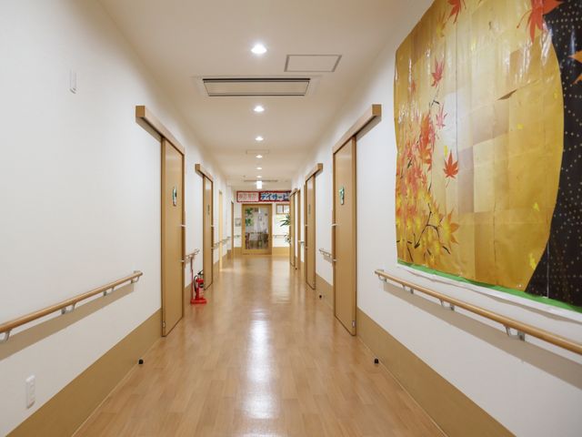 明るい廊下と和風の掛け軸 通路 ゆったりとした廊下は、床も壁も明るい色で統一され、和風の掛け軸が心安らぐ空間を演出しています。手すり沿いの歩行も安心です。