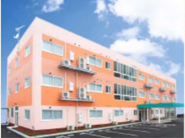 明るい色の建物の外観 外観 広々とした駐車場が見え、清潔感のある建物です。ここでの仕事は安心感をもたらすでしょう。