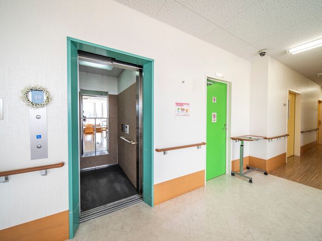 廊下と開いたエレベーター エレベーター 静かで明るい廊下に、手すりが設けられたエレベーターがあります。来訪者の利便性を高める配慮がされています。