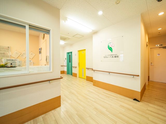 廊下の手すりと掲示物 受付 カラフルな扉が印象的な廊下です。手すりが設けられ、見やすい掲示物もあるため、日々の生活がサポートされます。