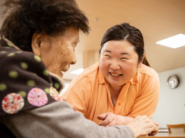 笑顔で対話するスタッフと利用者 スタッフ 明るい笑顔で利用者の話に耳を傾けるスタッフの姿から、温かなコミュニケーションが感じられます。