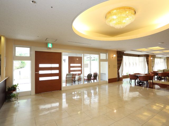 明るいエントランスホール 玄関出入口 天井のシャンデリアが煌めき、温かみのあるエントランスが迎えてくれます。ゆったりとした空間で利用者の憩いの場となることでしょう。