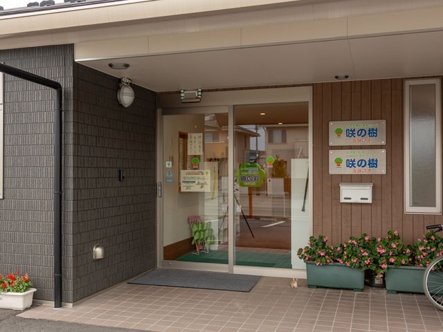 エントランスの様子 施設表示板 清潔感のあるエントランスは、訪れる人々を暖かく迎え入れます。ガラス戸越しに見える緑の椅子が、心を和ませる空間を演出しています。
