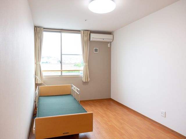 居室のベッドと窓 居室 広々とした明るい居室で、窓からは自然光が差し込みます。皆様の快適な生活空間を提供しております。