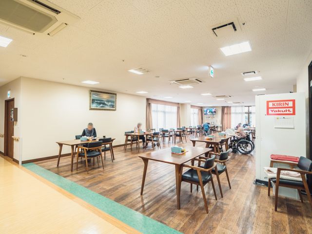 広々とした共有ダイニング リビング 明るく広々としたダイニングで、来訪者はゆったりと食事や読書を楽しんでいます。テーブルごとに十分なスペースがあり、快適です。