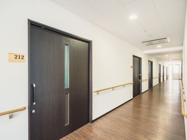 清潔な廊下の一角 居室 手すりつきの廊下を歩けば、居住者の安全と快適な移動が保証されています。あたたかみのあるデザインが、皆さんをお待ちしています。